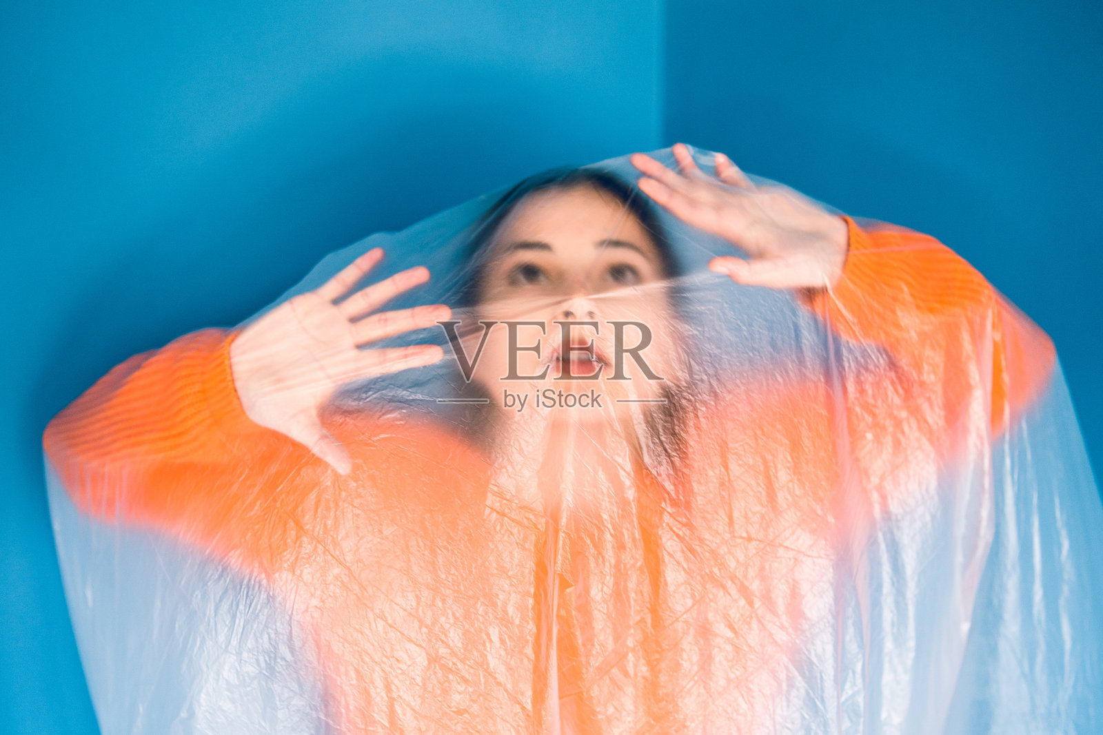 身穿橙色肖像的年轻女子前面挂着蓝色尼龙塑料袋的墙壁，是环保环保拯救地球海洋的生态理念照片摄影图片