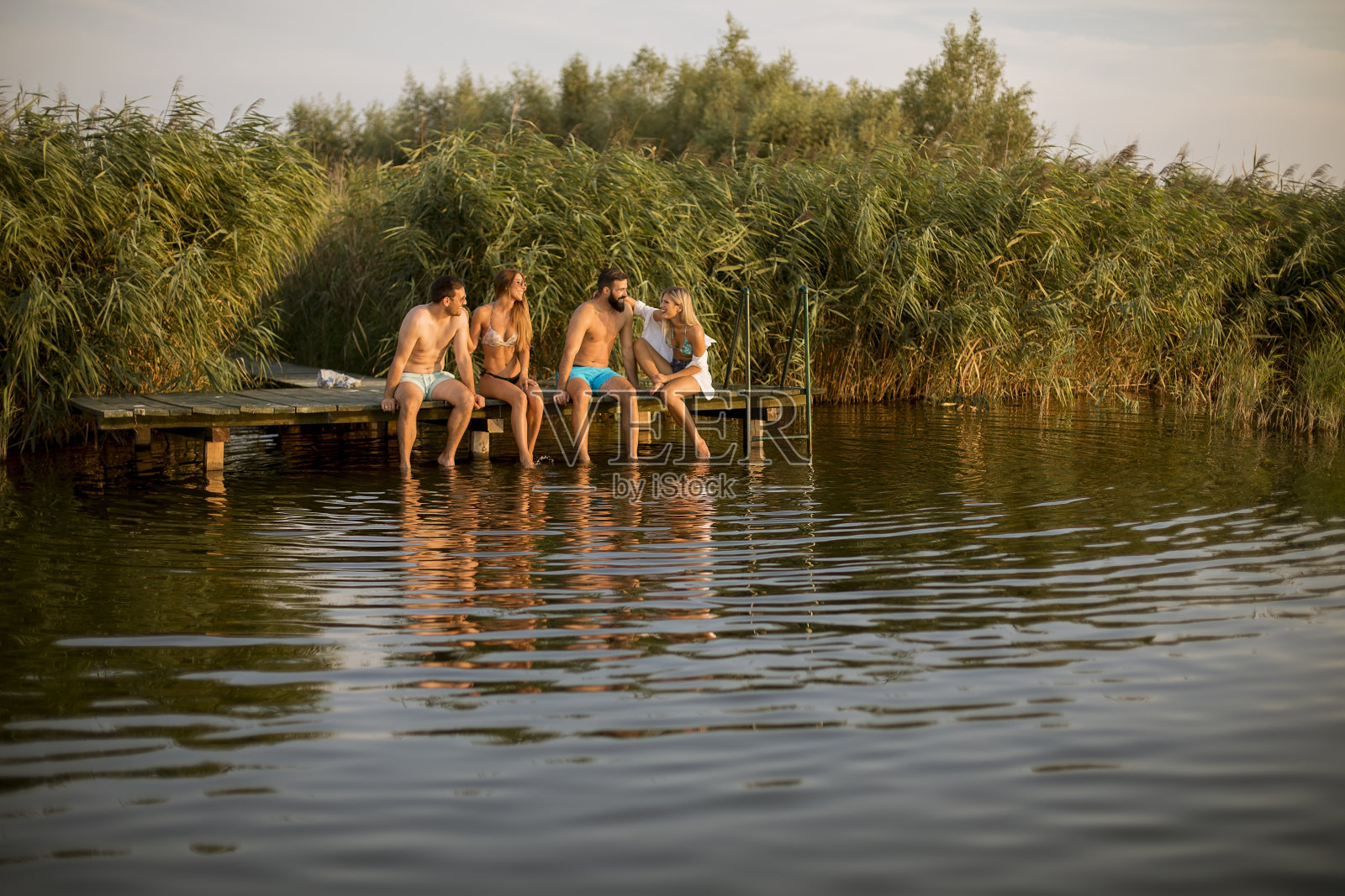 快乐的年轻朋友们坐在湖边的码头上照片摄影图片