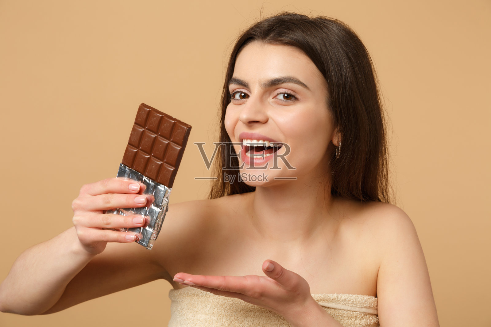 近女人20多岁与完美的皮肤，化妆hold巧克力条孤立的米黄色粉彩墙背景，工作室肖像。保健美容程序概念。模拟拷贝空间。照片摄影图片