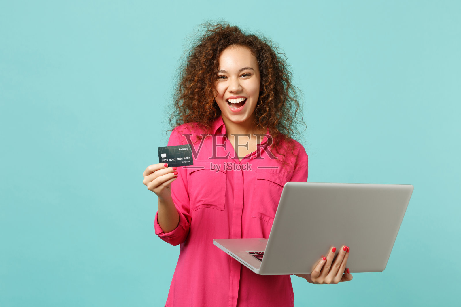 笑眯眯的非洲女孩穿着休闲衣服用笔记本电脑电脑，拿着信用卡孤立在蓝绿色背景的工作室里。人真诚情感生活理念。模拟拷贝空间。照片摄影图片