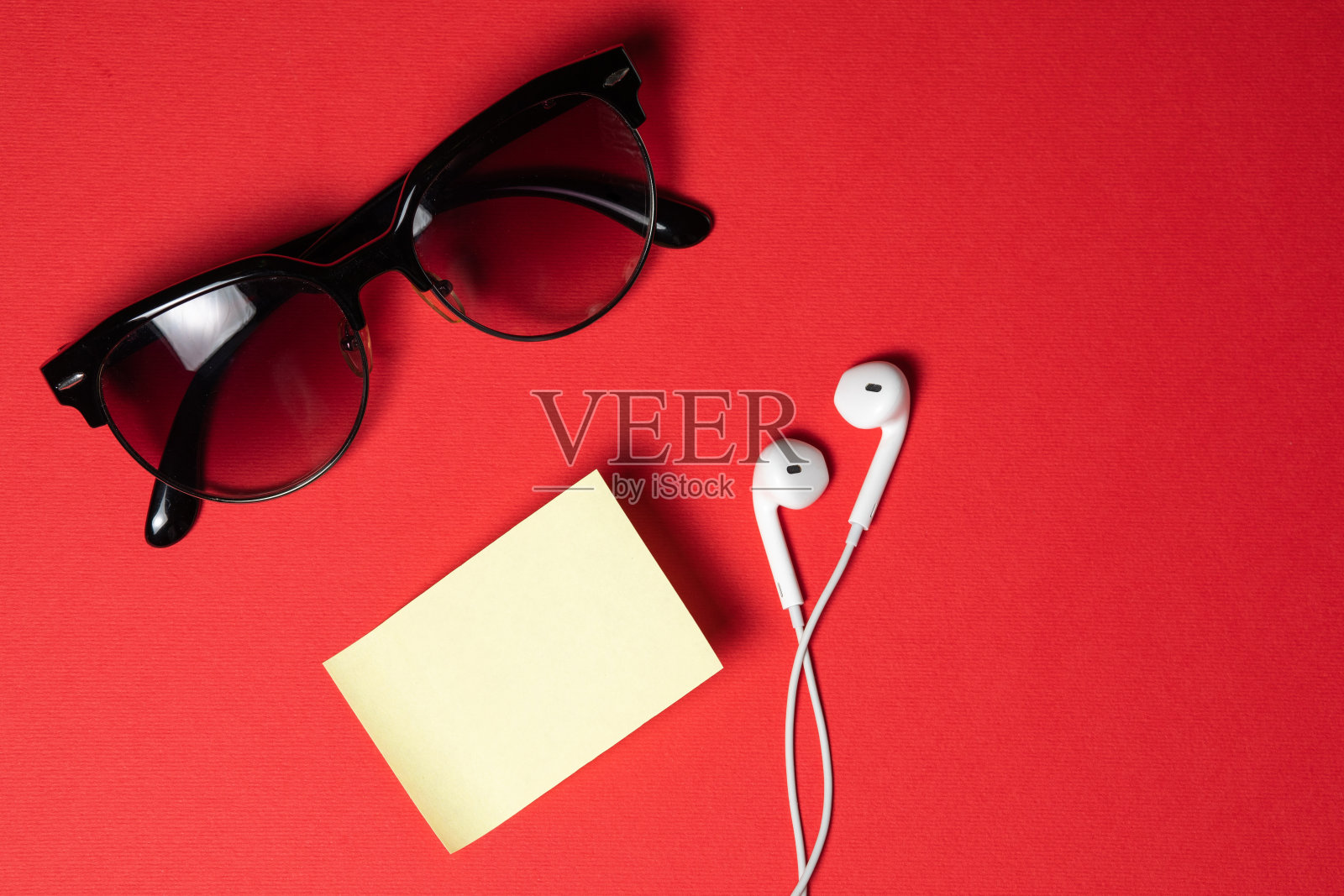 黑屏智能手机通过红色背景顶视图螺旋线连接耳机，太阳镜照片摄影图片