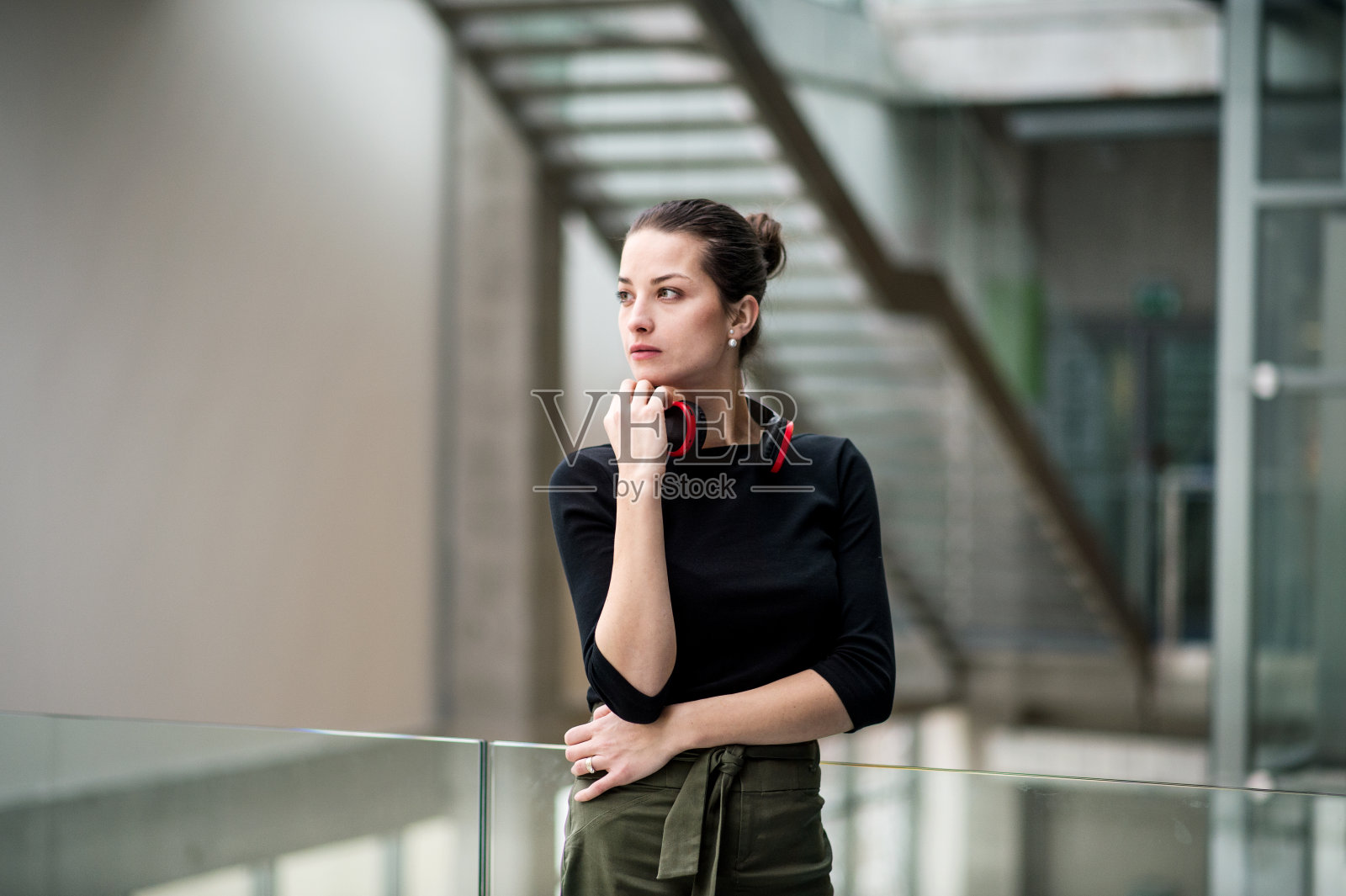 一幅年轻女商人戴着耳机站在办公室外的走廊里的肖像。照片摄影图片