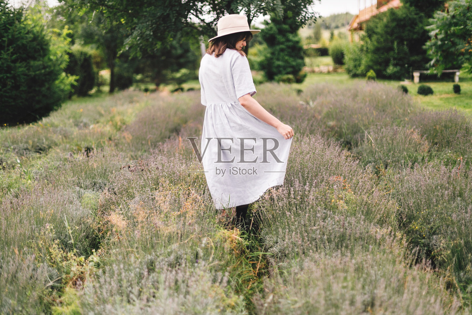 时髦的时髦女孩在亚麻裙和帽子走在薰衣草的田野和放松。快乐的波西米亚女人享受薰衣草的香气在夏天的山。大气平静的乡村时刻照片摄影图片