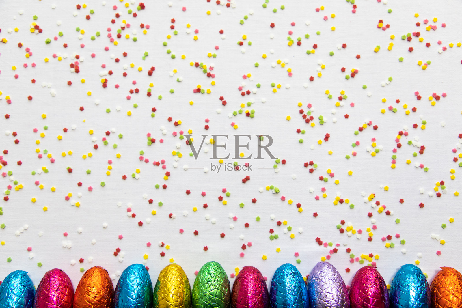 许多人在白色背景和五彩纸屑上排列彩色巧克力复活节彩蛋照片摄影图片