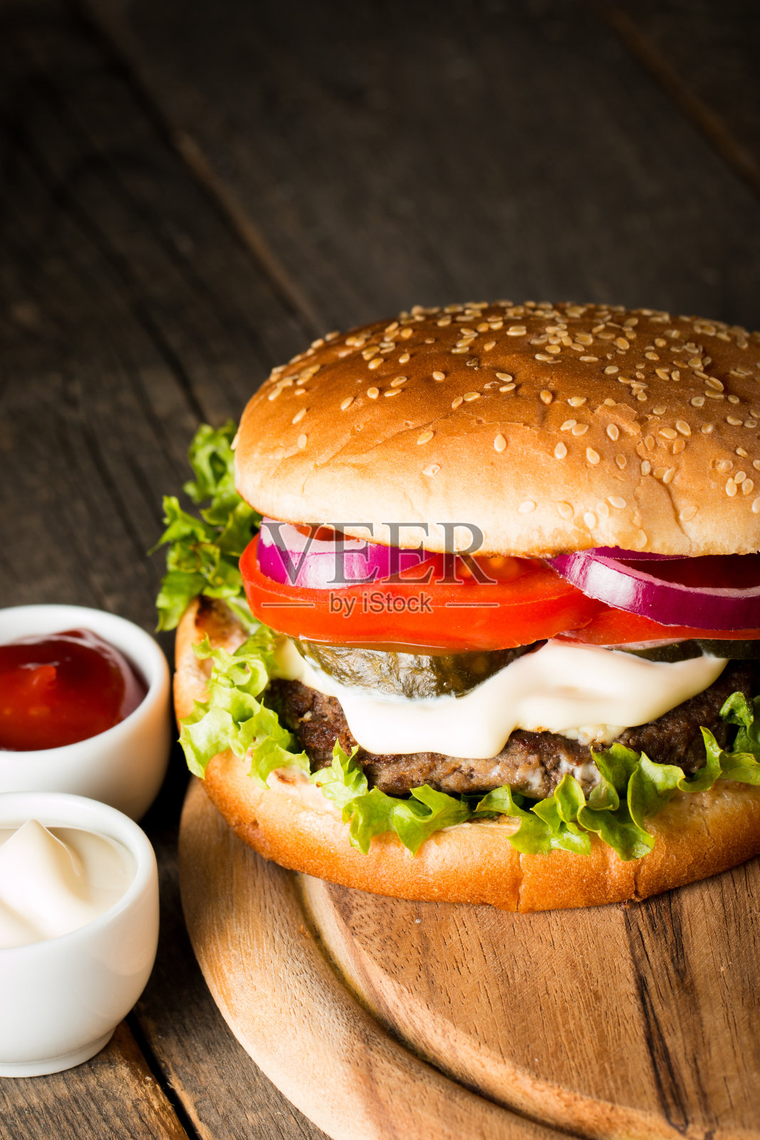 自制汉堡的特写照片，啤酒由牛肉、洋葱、番茄、生菜、奶酪和香料制成。新鲜的汉堡特写在木制的乡村桌子和土豆薯条和薯条。照片摄影图片