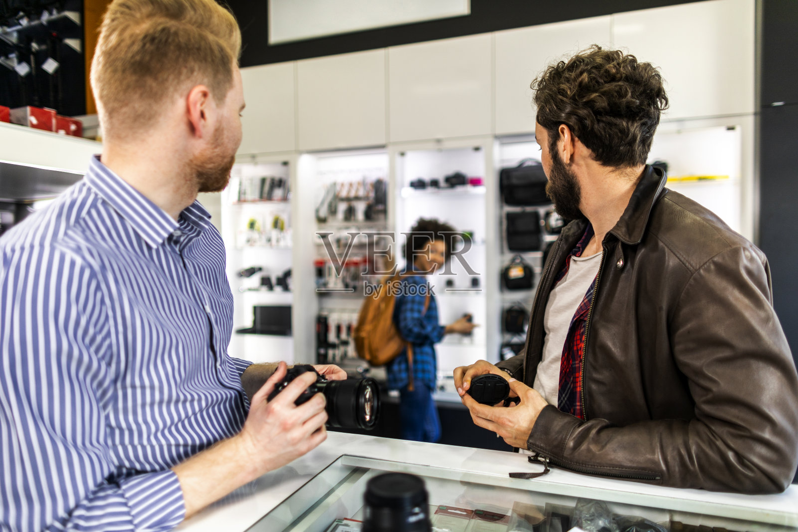 店主帮助一个年轻的顾客夫妇，因为他们正在浏览一个相机设备商店照片摄影图片