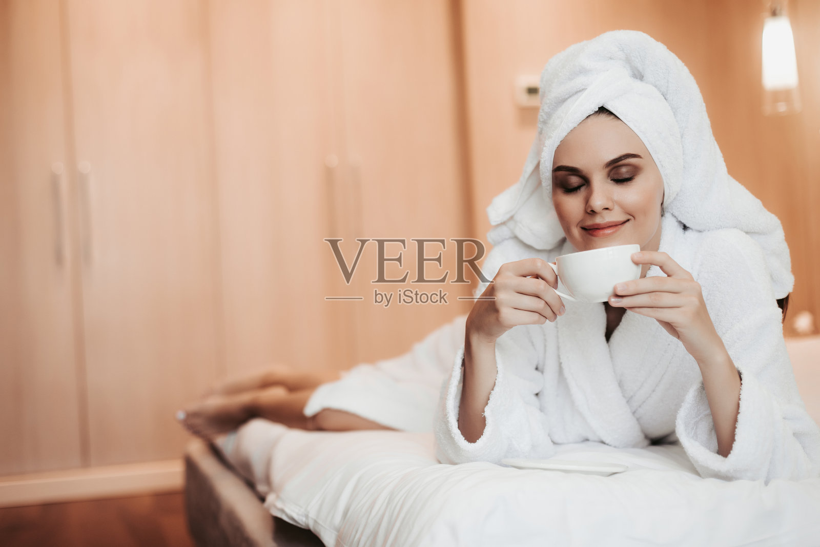 年轻女子在浴衣躺在床上与茶照片摄影图片