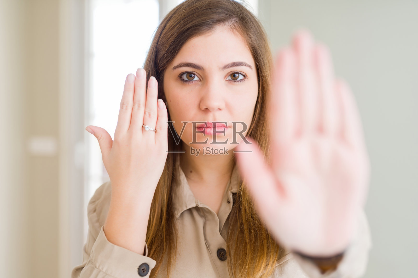 美丽的年轻女子展示手上的订婚戒指与张开的手做停止标志与严肃和自信的表情，防御手势照片摄影图片