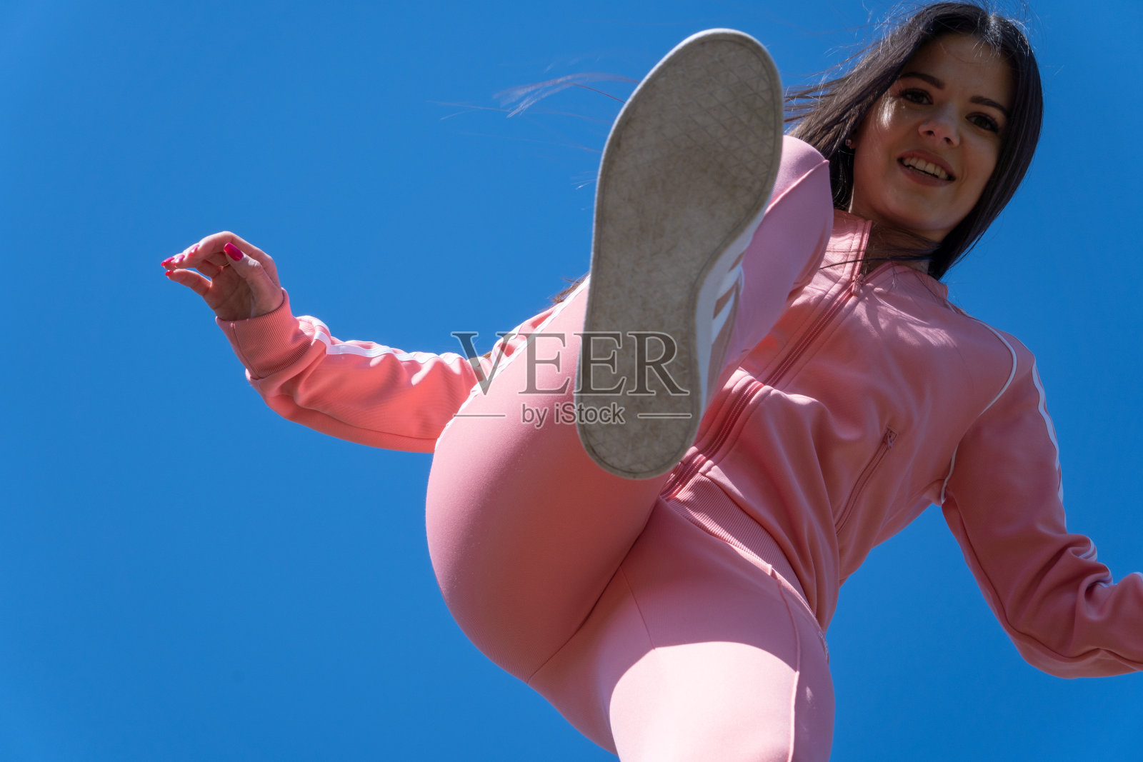 蓝色天空下穿着粉色运动服的女孩。照片摄影图片