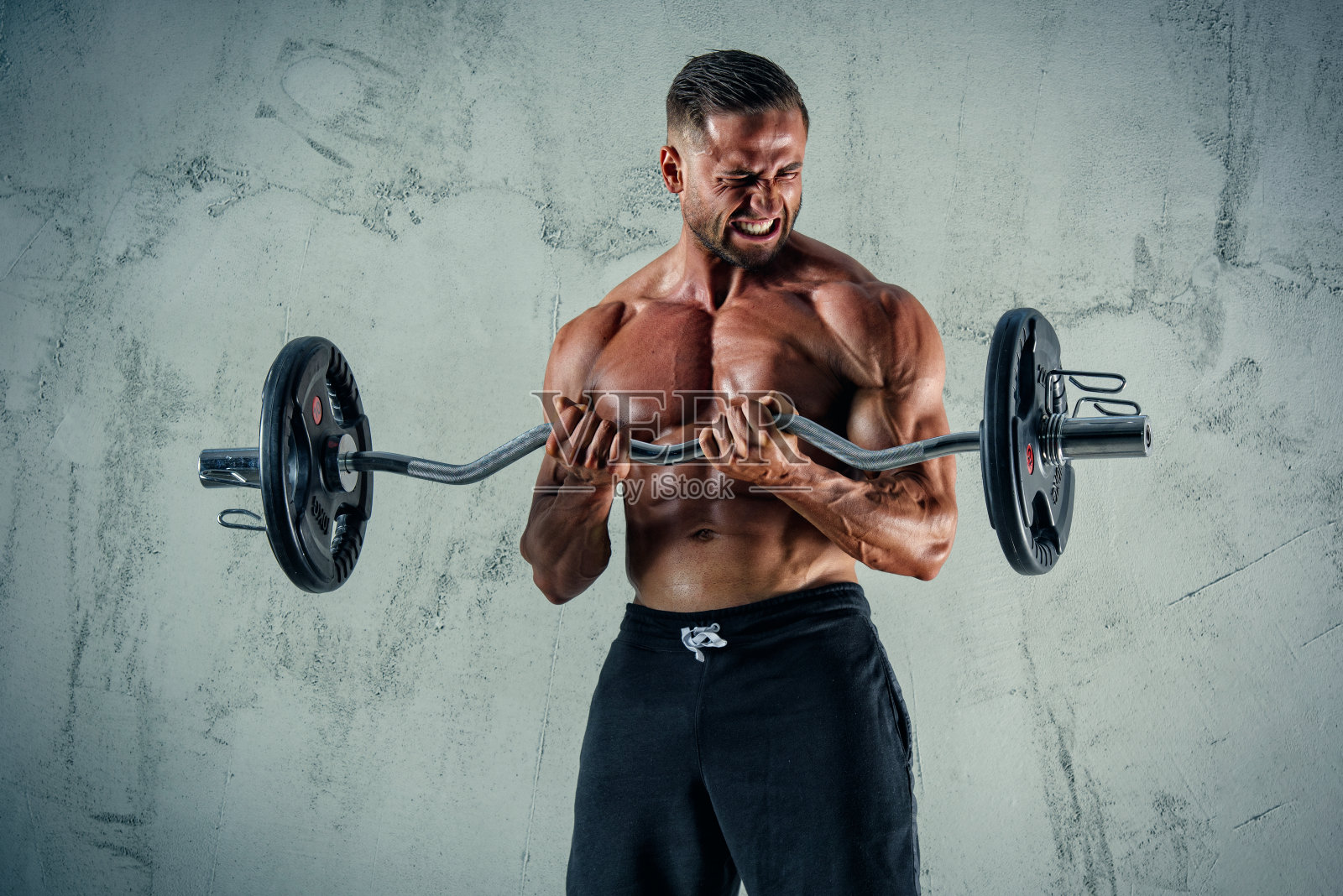 肌肉男用重量来锻炼。他正在用哑铃和杠铃表演二头肌照片摄影图片