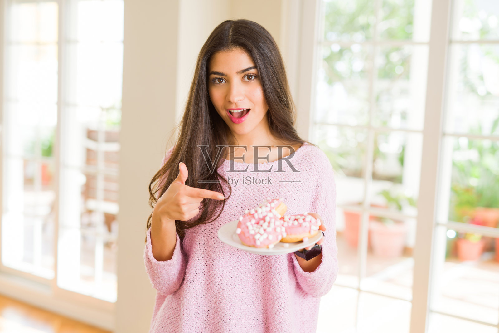 漂亮的年轻女子微笑着拿着一盘美味的粉色甜甜圈照片摄影图片