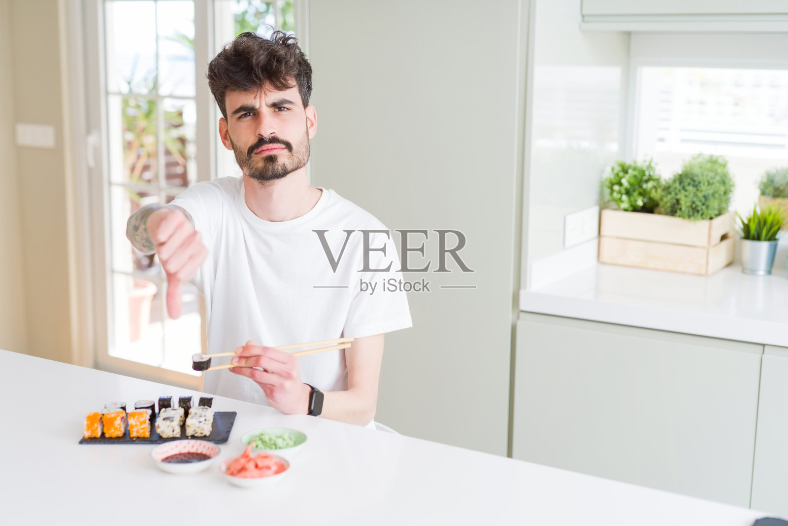 一名年轻人在吃送上门的亚洲寿司时面带怒色，用大拇指表示不喜欢，拒绝的概念照片摄影图片