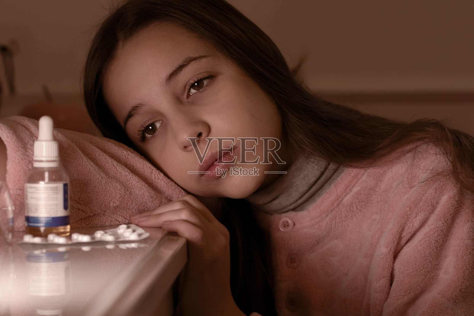 一个患流感的少女正拿着药片和一瓶药水坐在桌子旁。治疗和治愈的概念。照片摄影图片