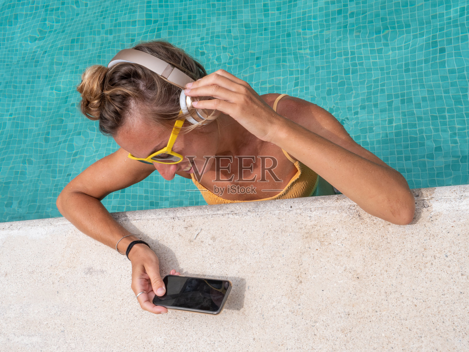 快乐的女人戴着耳机在游泳池里听音乐照片摄影图片