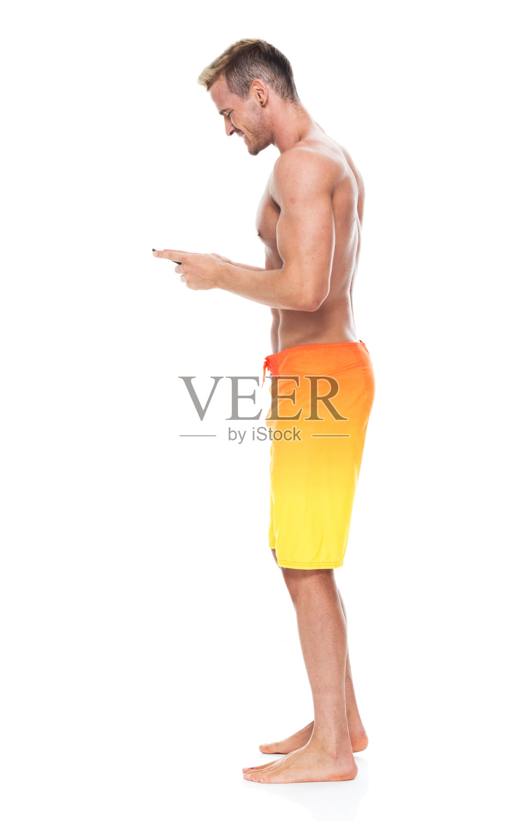 帅气的男人赤裸上身，穿着短裤，在智能手机上发短信照片摄影图片