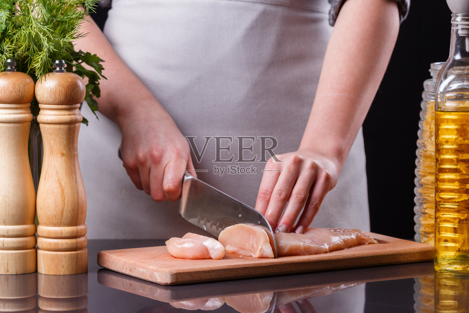 穿着灰色围裙的年轻女子正在切鸡胸肉照片摄影图片