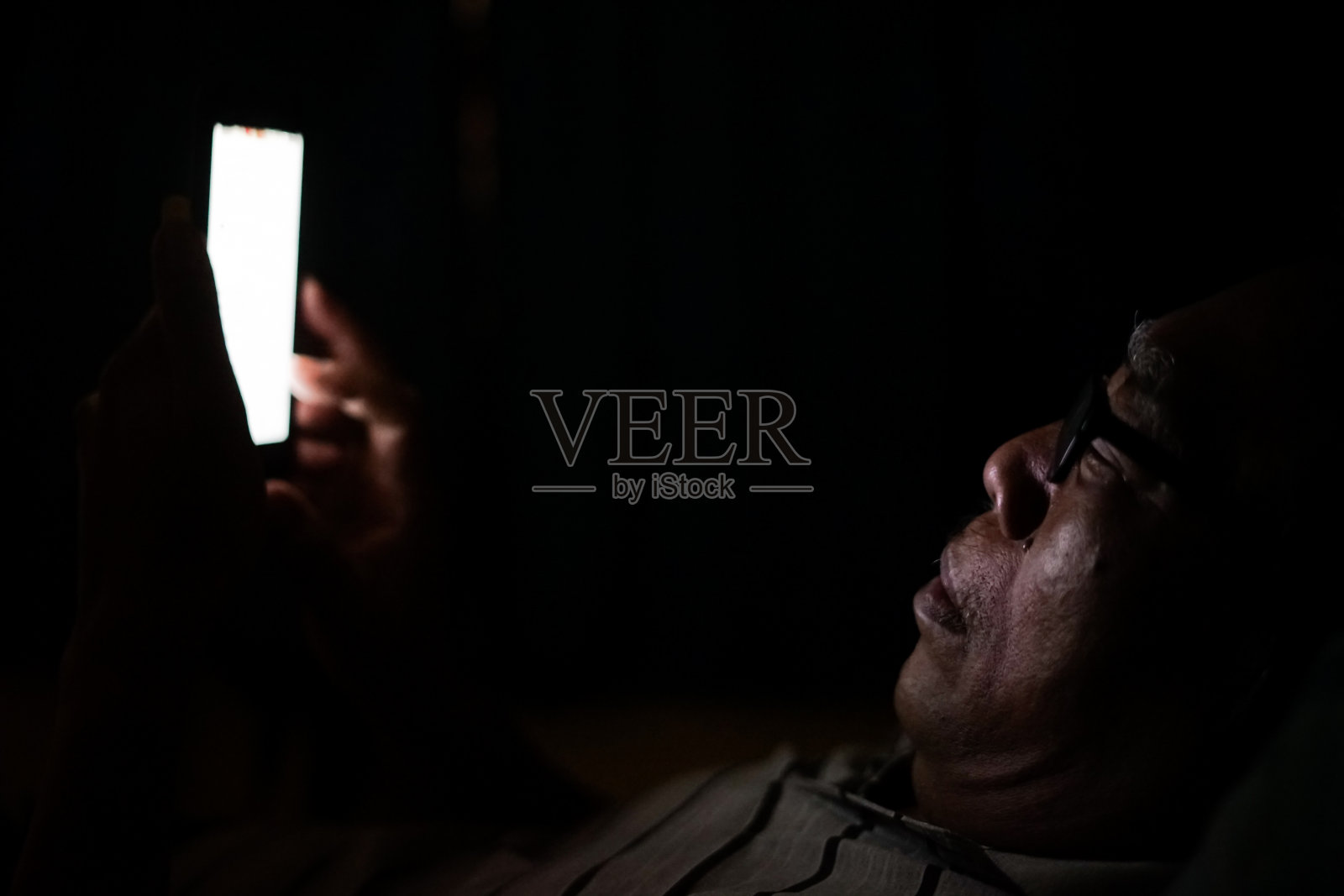 在黑暗房间里玩智能手机的老年亚洲男人照片摄影图片