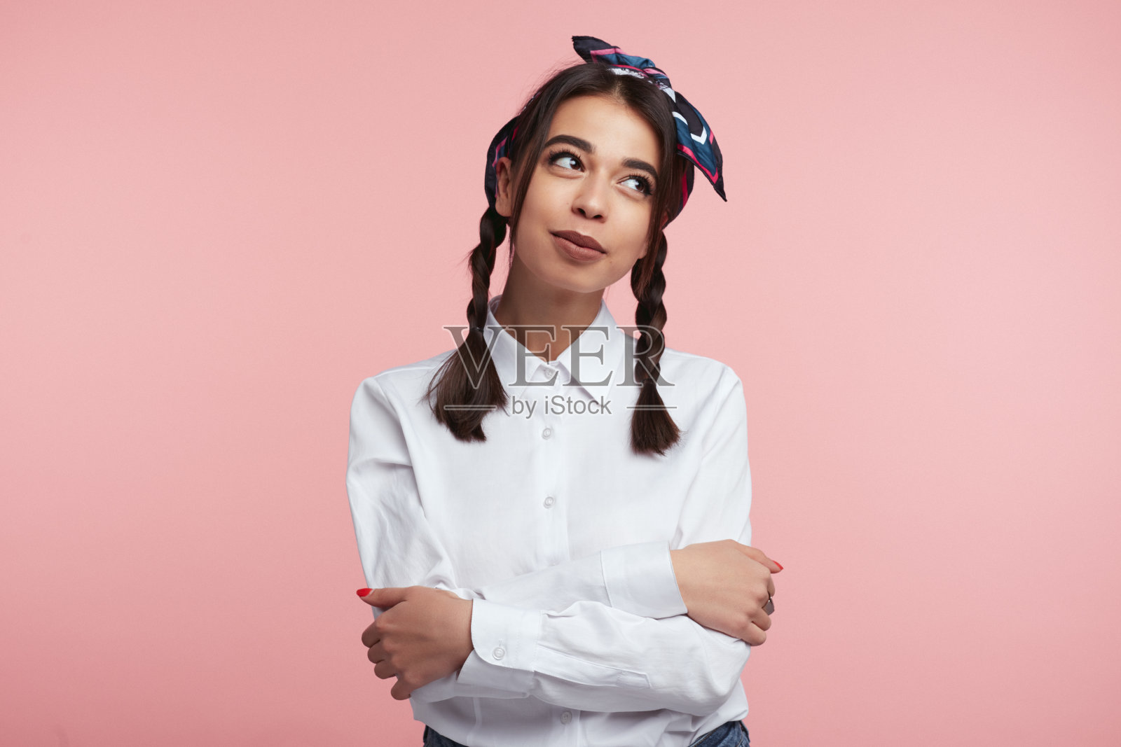 近距离的幸福的女性与交叉的胳膊和灿烂的笑容在脸上，穿着白色的衬衫和头巾，孤立在粉红色的墙照片摄影图片