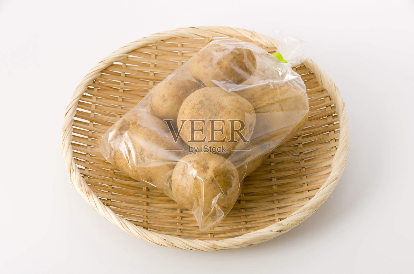 白底竹制滤锅，装于塑料袋内的马铃薯照片摄影图片