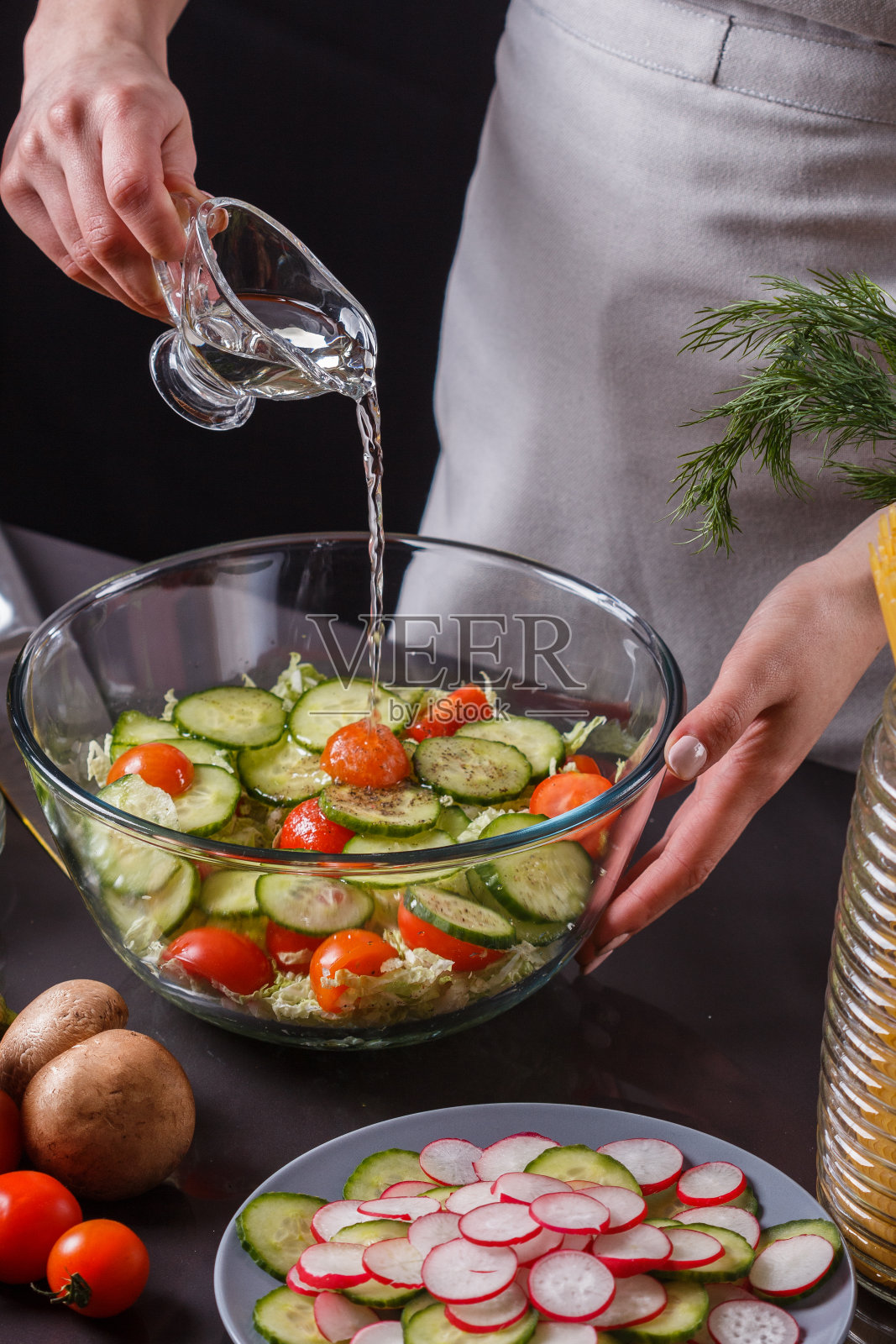 一位穿着灰色围裙的年轻女子正在给卷心菜沙拉加醋照片摄影图片