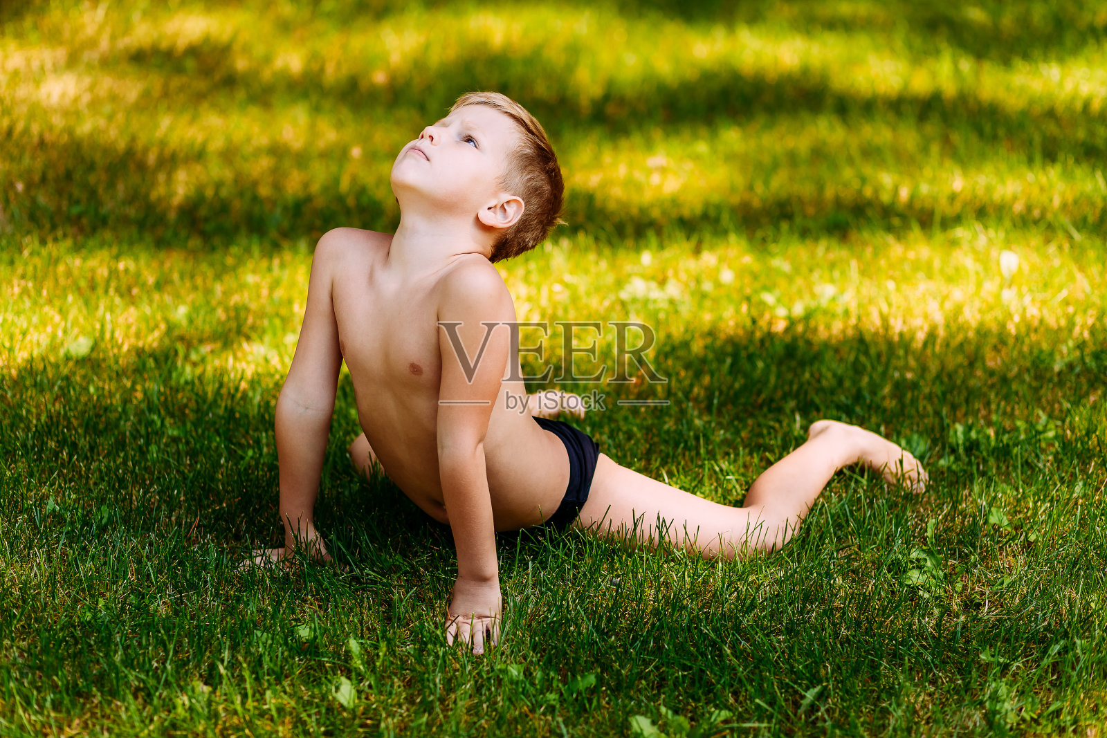 7岁柔韧的孩子穿着泳裤在夏天的绿草地上做杂技运动。照片摄影图片