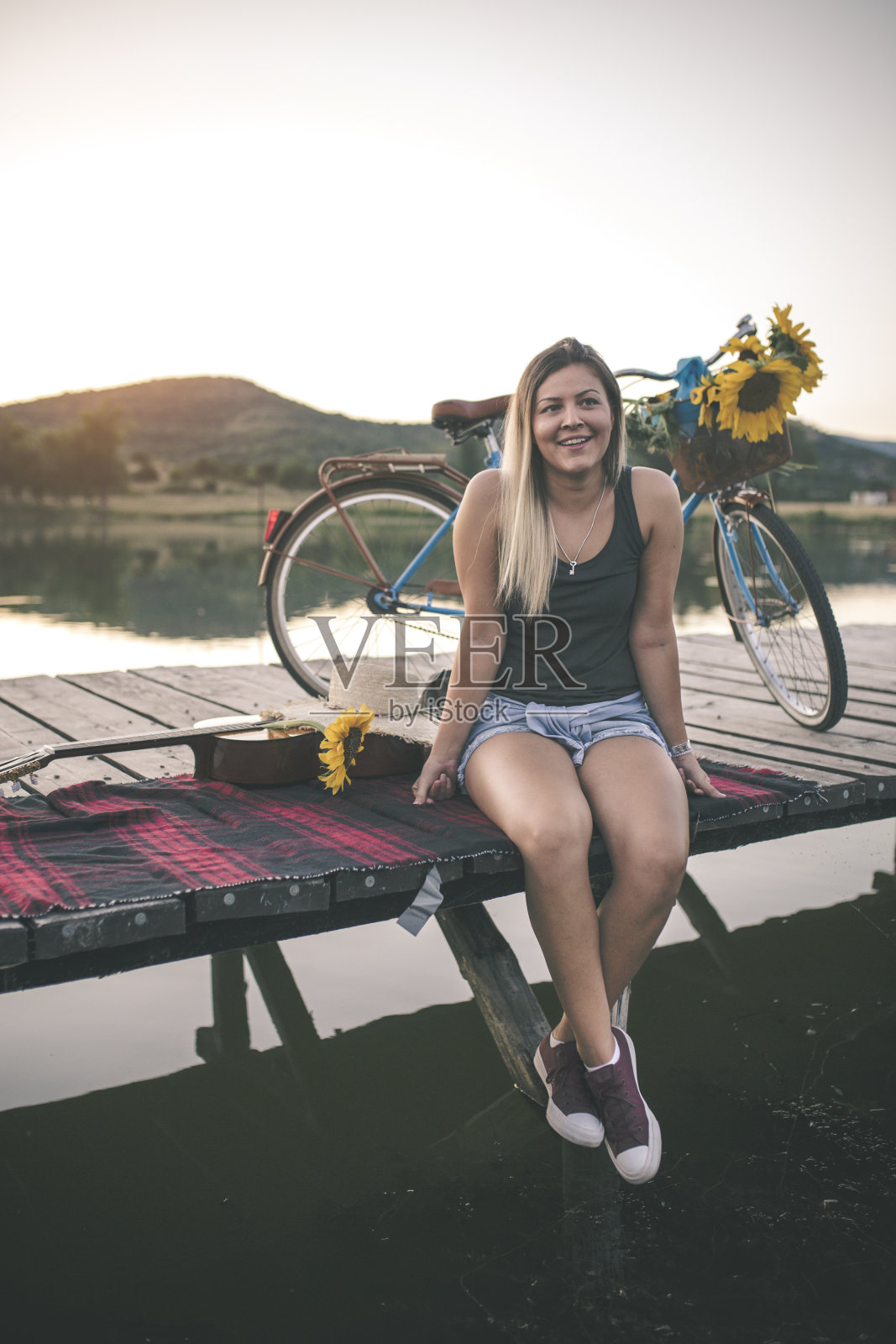 一个女人坐在老木头码头上，看着湖面照片摄影图片