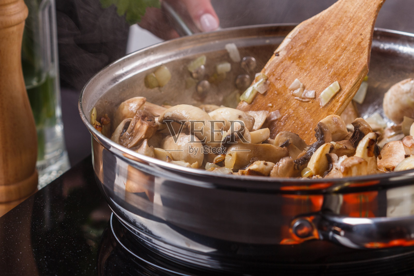 穿着灰色围裙的年轻女子用煎锅烤蘑菇照片摄影图片