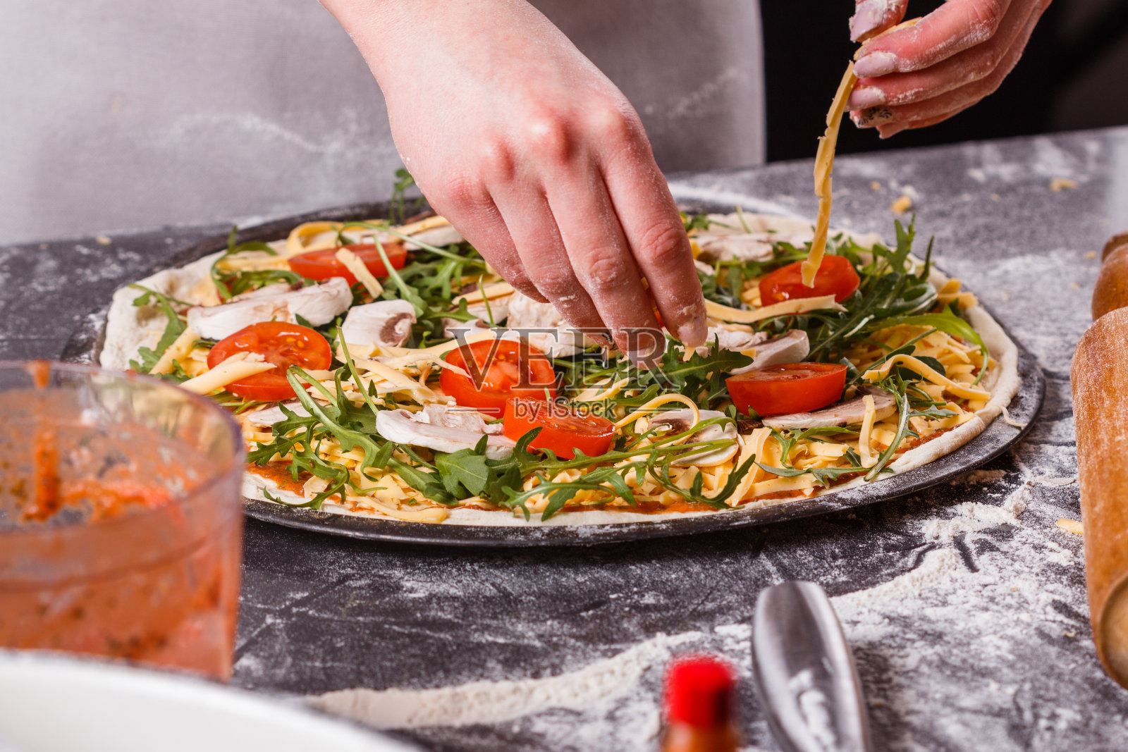 穿着灰色围裙的年轻女子正在准备素食披萨照片摄影图片