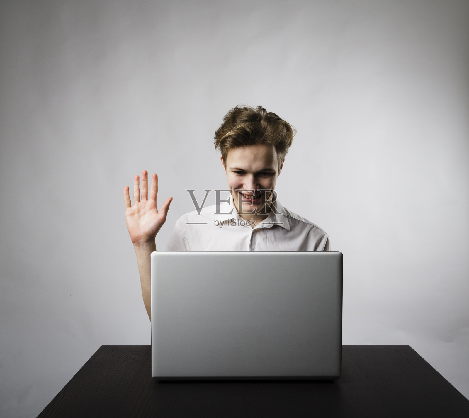 年轻人用笔记本电脑浏览网络。挥舞的手。聊天的概念。年轻人向手提电脑挥手。照片摄影图片