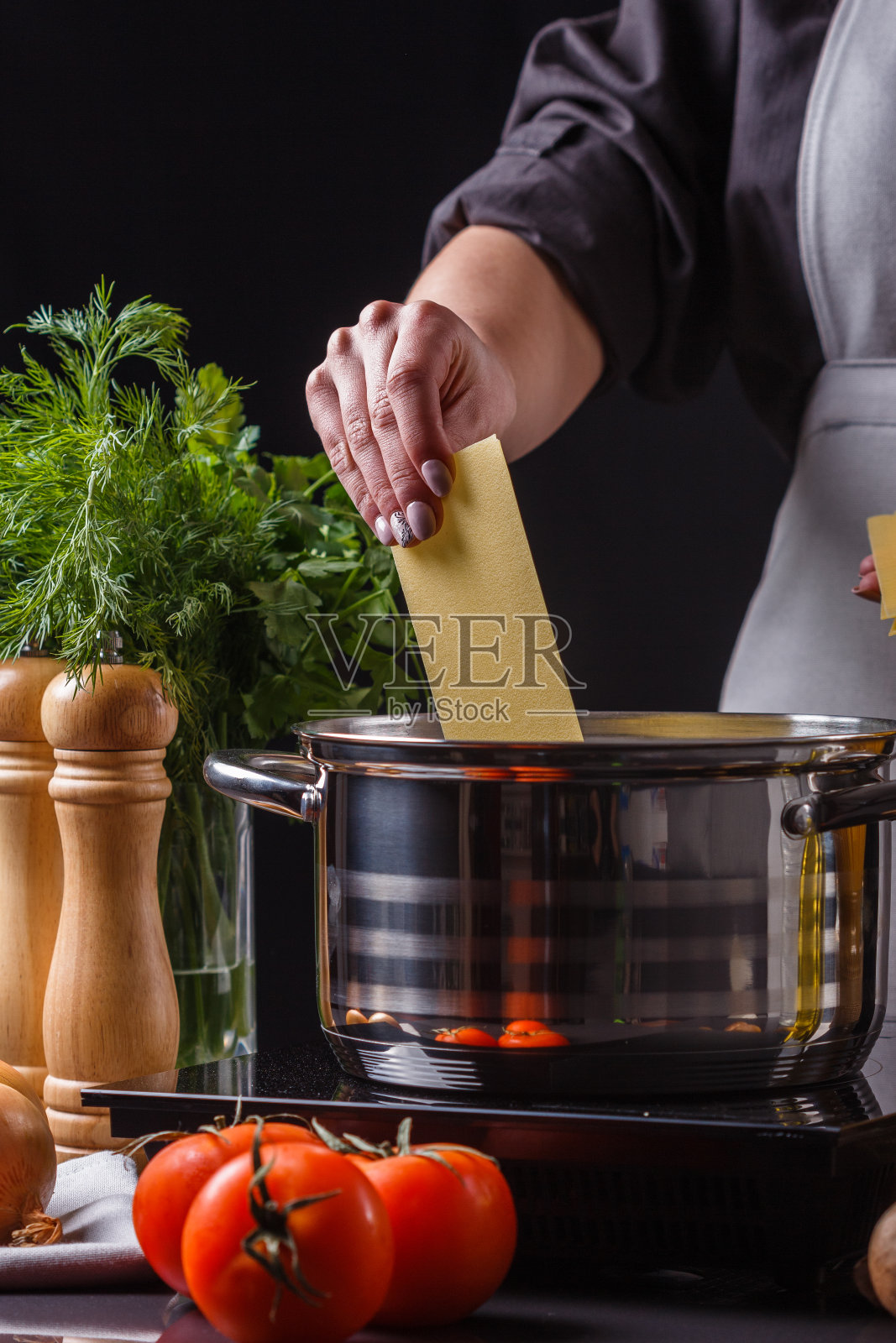 穿着灰色围裙的年轻女子在做意大利面照片摄影图片