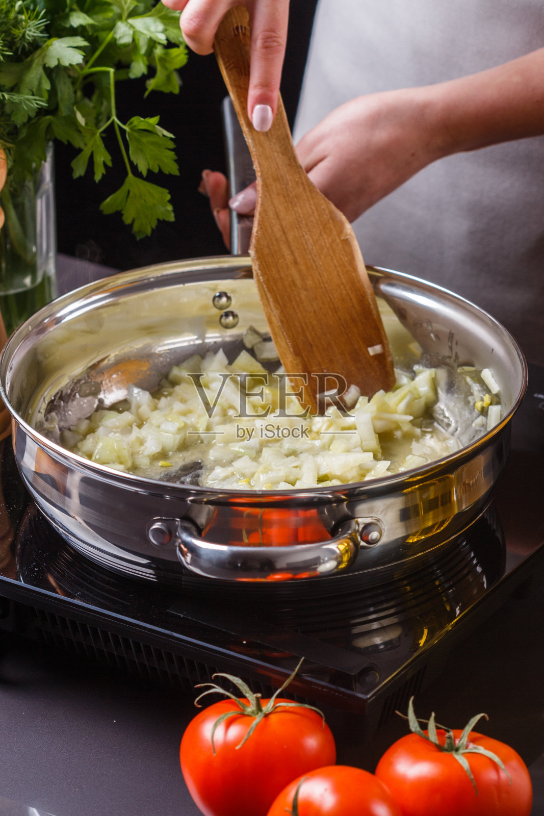 穿着灰色围裙的年轻女子在煎锅里烤洋葱照片摄影图片