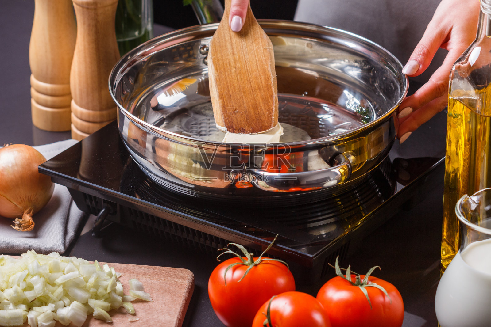 一位穿着灰色围裙的年轻妇女在煎锅里放黄油照片摄影图片