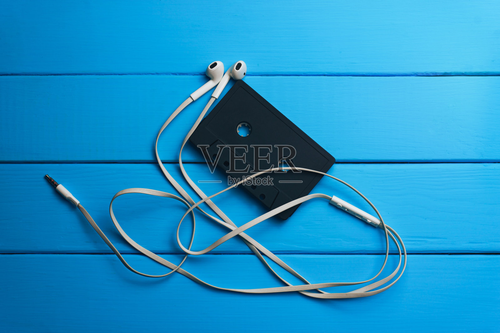 黑色经典磁带和白色耳机在蓝色木制桌子的背景。照片摄影图片