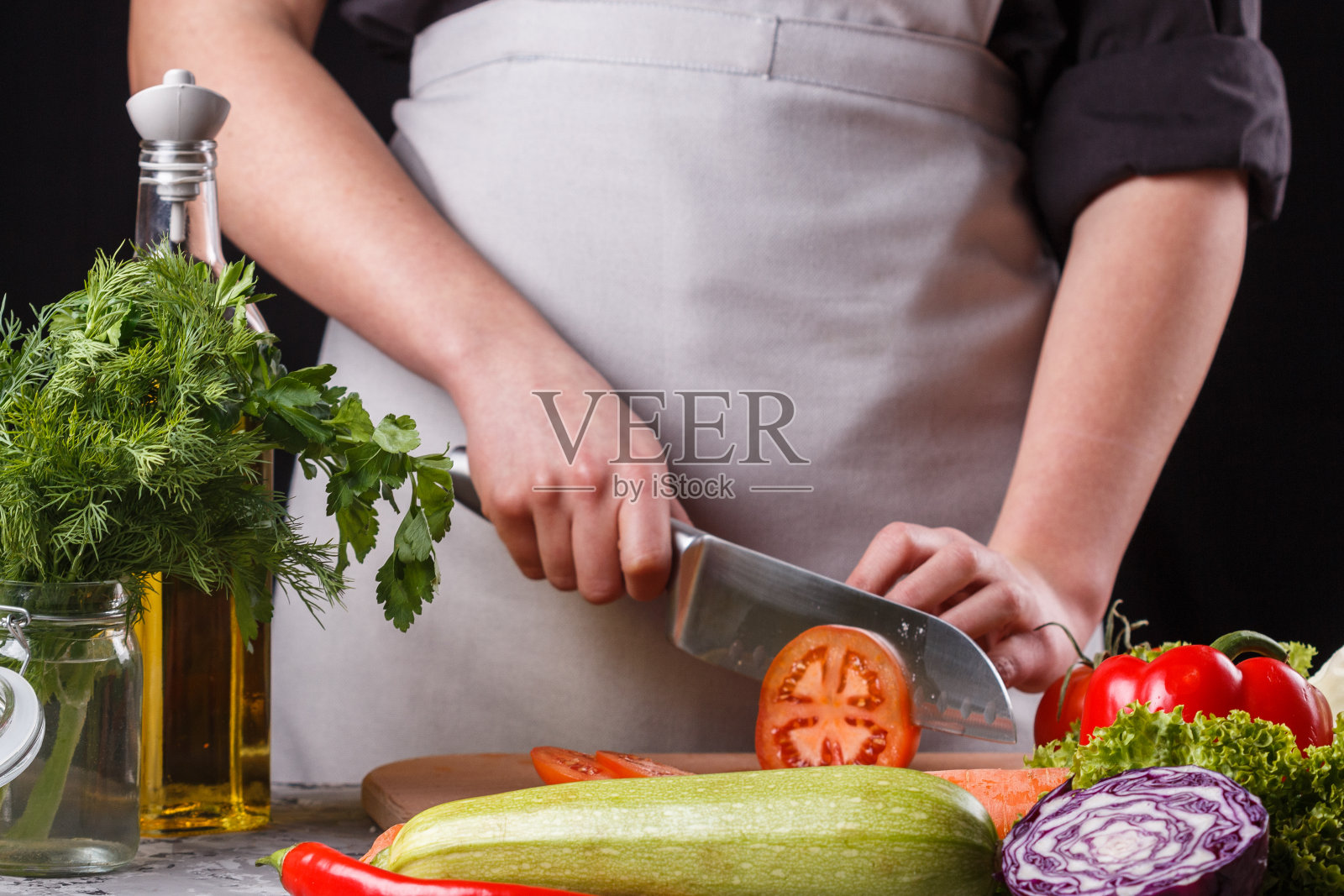 穿着灰色围裙正在切番茄的年轻女子照片摄影图片