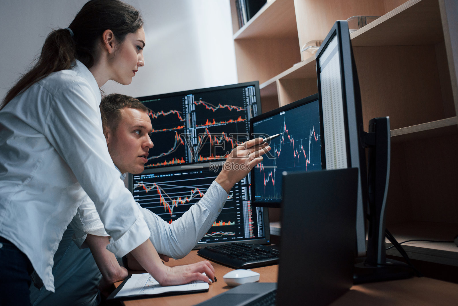 高而漂亮的结果。一组股票经纪人正在一间有多个显示屏的办公室里进行对话。照片摄影图片