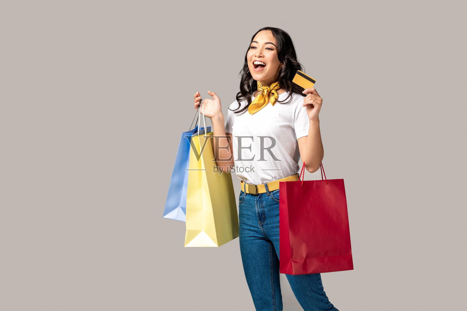 微笑美丽的亚洲女人携带彩色购物袋和持有信用卡孤立在灰色照片摄影图片