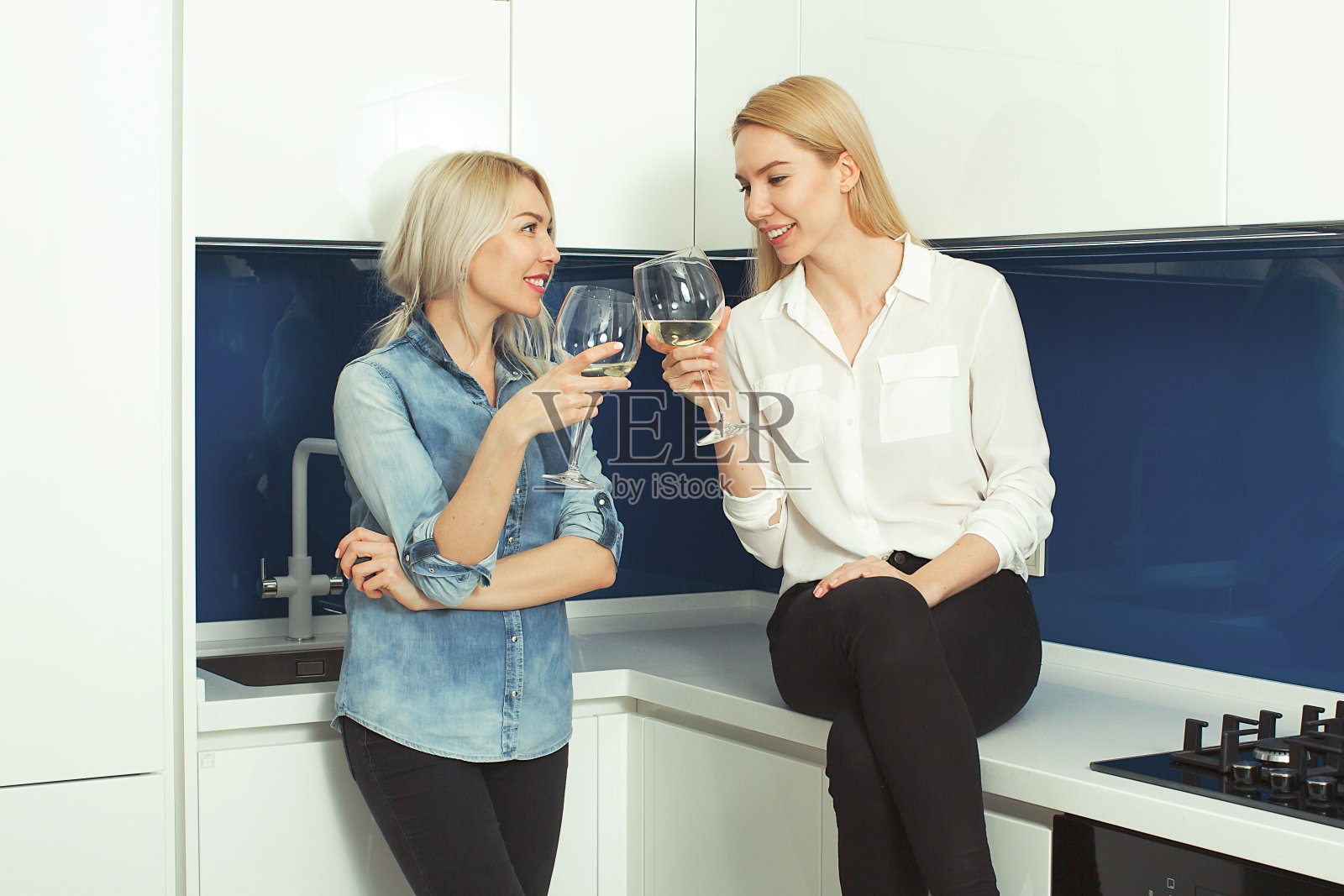 两个金发女友在厨房喝酒并大笑。两个成年姐妹在厨房拿着酒杯照片摄影图片