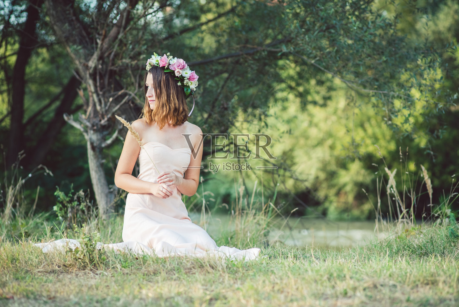 年轻的白人妇女穿着白色的衣服，戴着花环坐在草地上。照片摄影图片