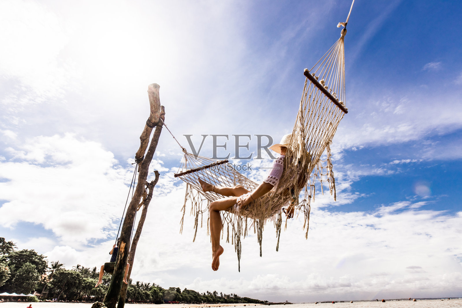 下图是无忧无虑的女人在沙滩上的吊床上放松。照片摄影图片