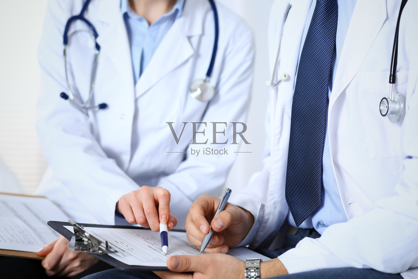 两个不知名的医生在填写医疗表格，特写的手。医生向病人提问或讨论药物治疗方案。医疗、保险和医学概念。照片摄影图片