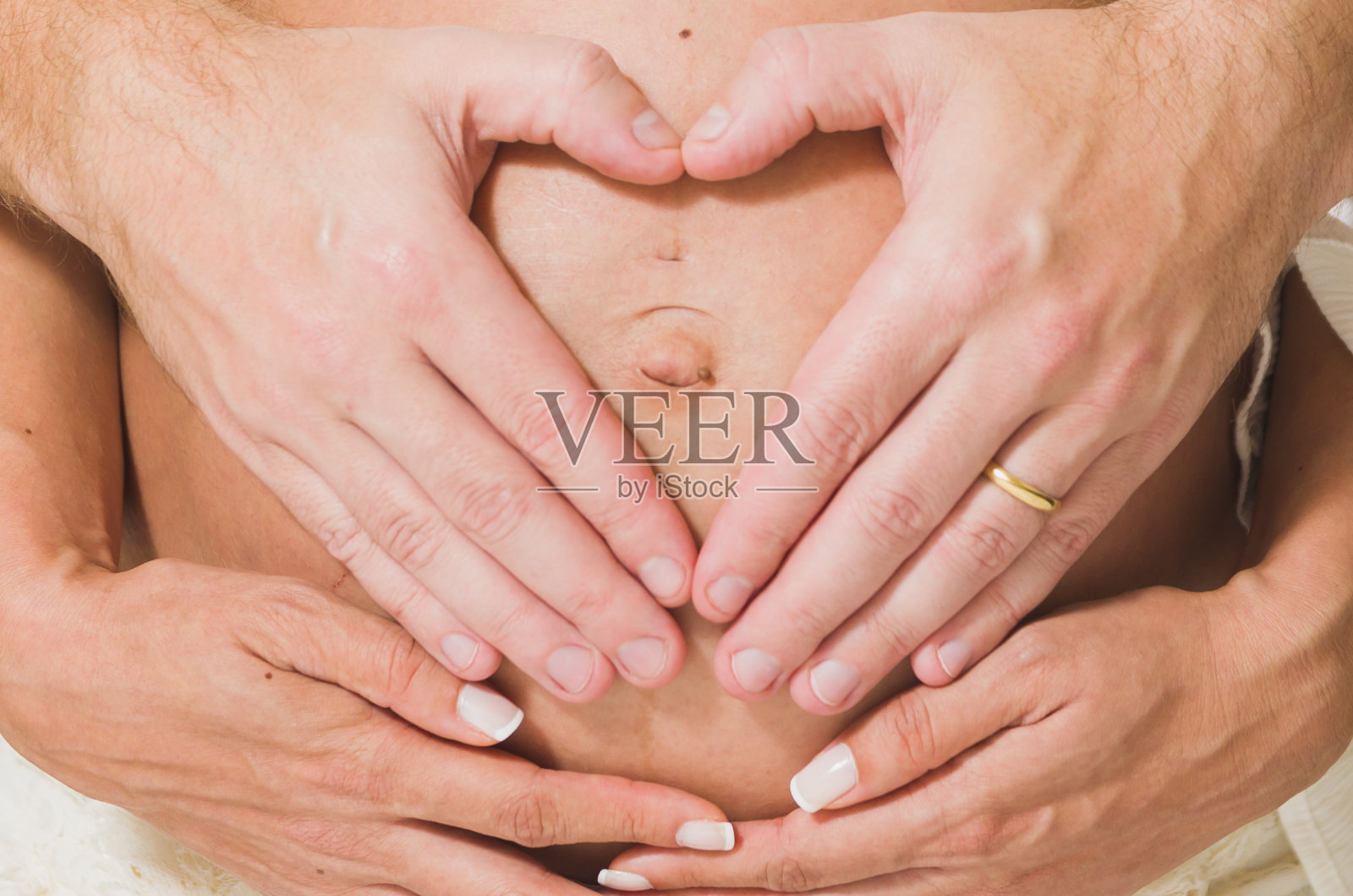 丈夫抚摸怀孕妻子的肚子，夫妻在家中用手比心照片摄影图片