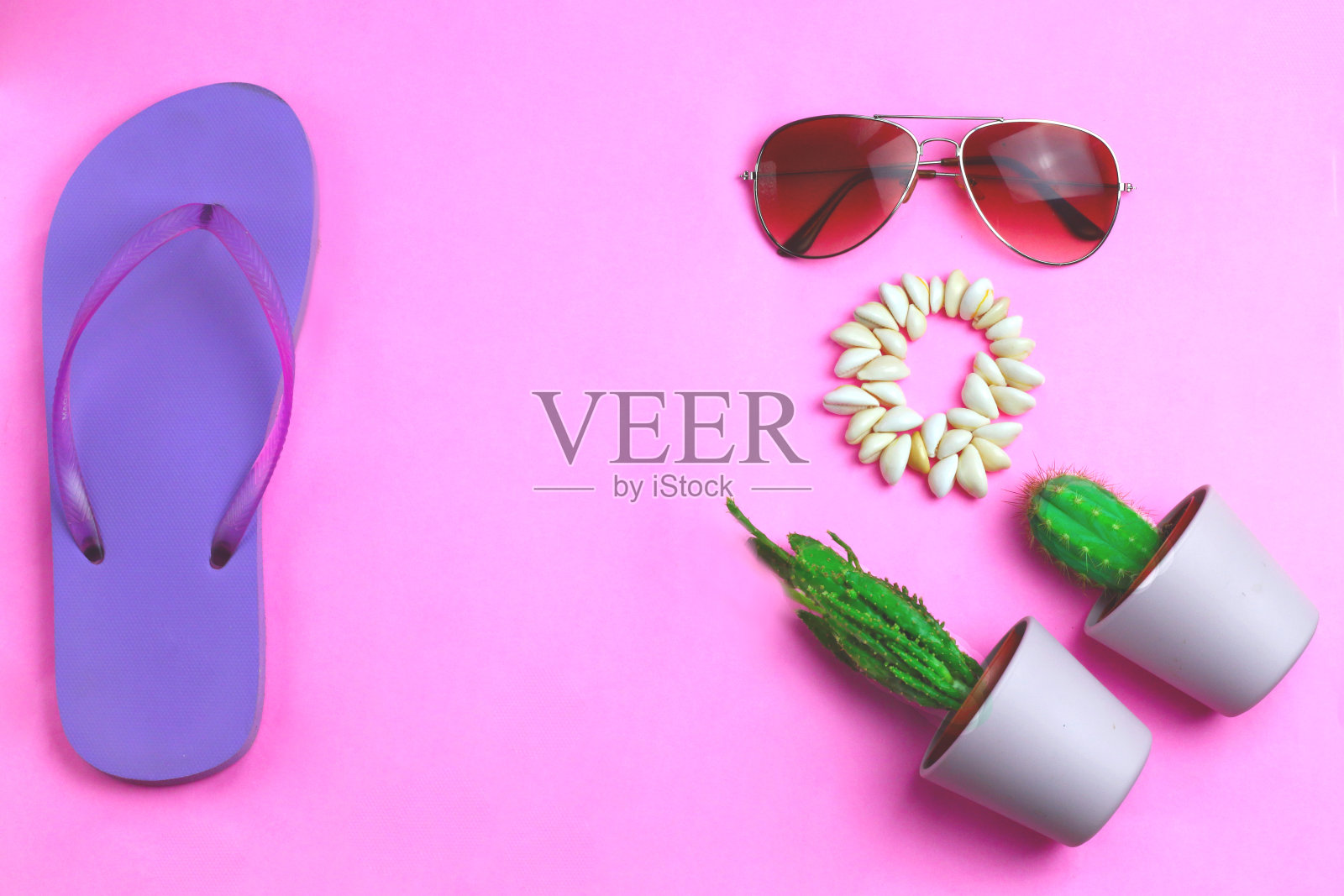 沙滩紫色人字拖，飞行员太阳镜，贝壳手镯和多汁仙人掌在粉红色的背景。夏日缤纷的旅游海滩平躺着照片摄影图片