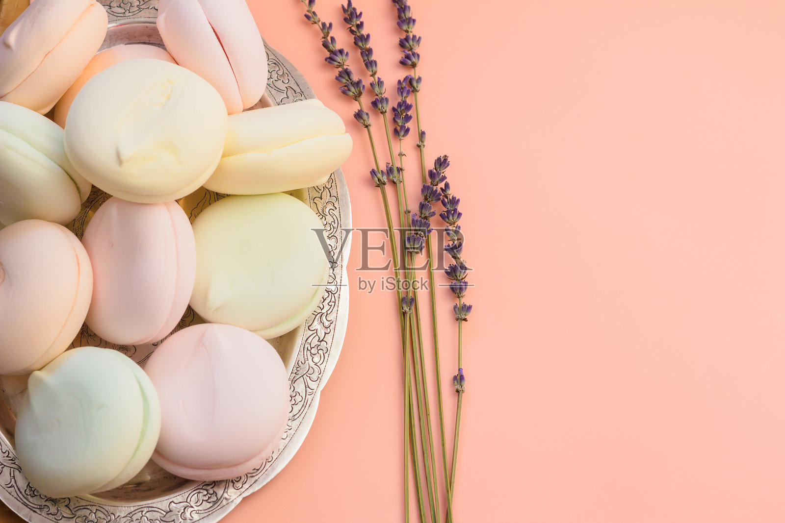 浅盘上放着棉花糖，浅粉色的背景上点缀着薰衣草花。照片摄影图片