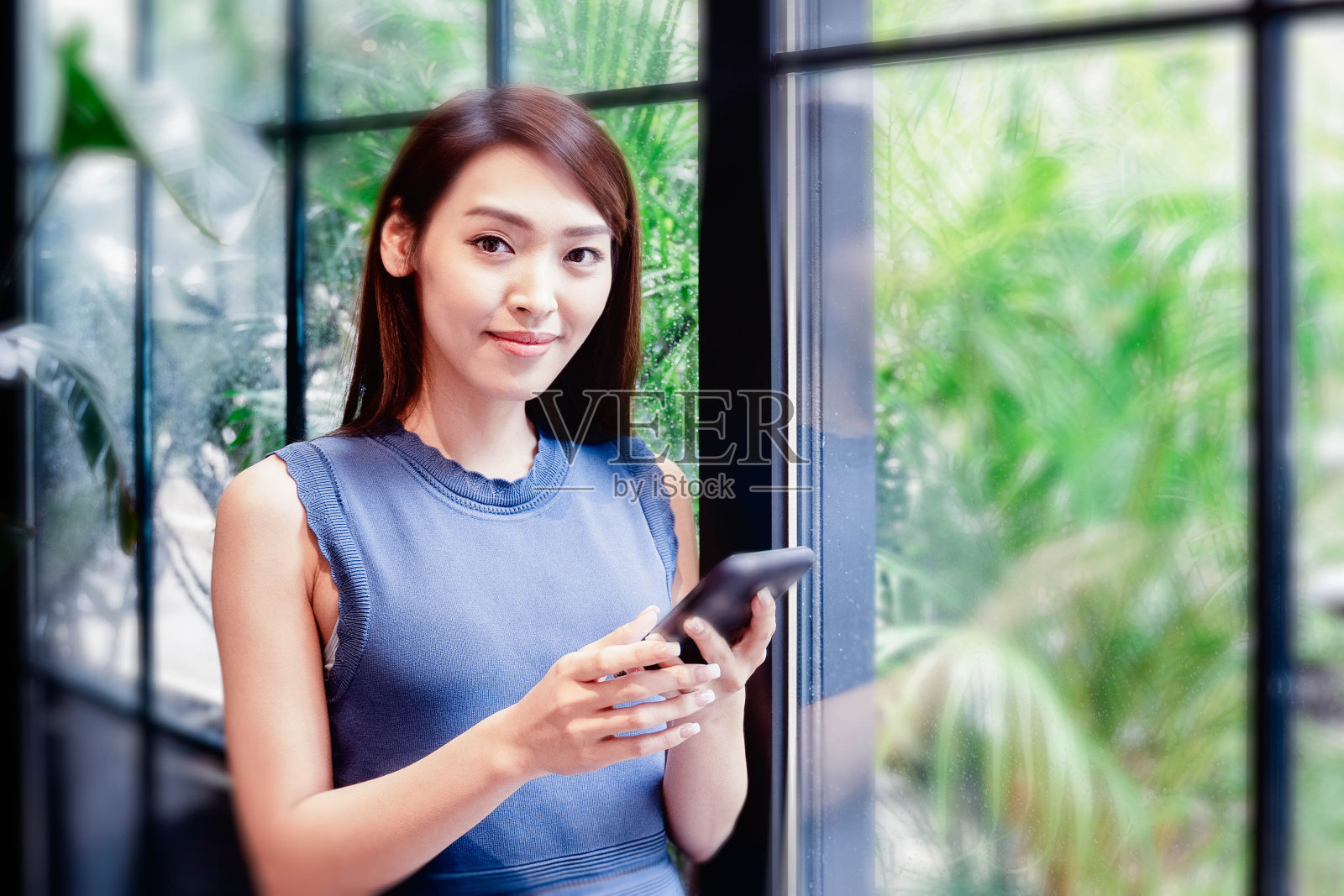 年轻的亚洲女人看着手机在一个现代的共同工作的办公室照片摄影图片