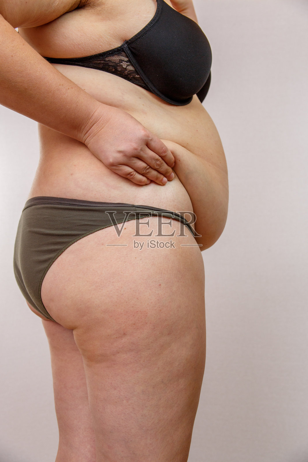 女人捏她的肚子，女孩捏她肚子上的脂肪，腹部的脂肪褶皱照片摄影图片