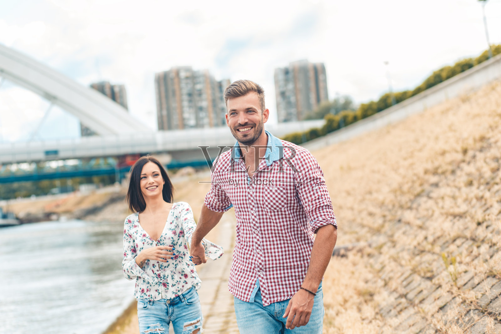 一对美丽的夫妇在河边散步，手牵着手。照片摄影图片