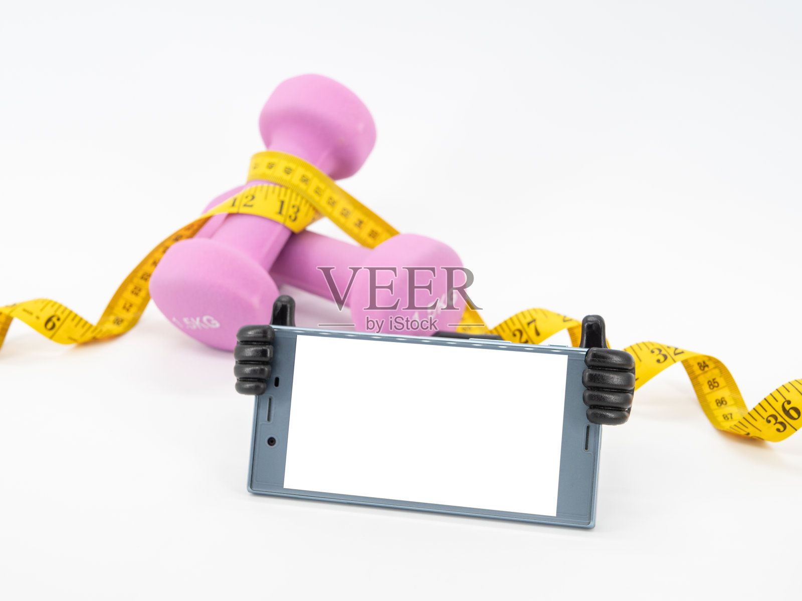 健身器材配有哑铃、卷尺和智能手机，屏幕空白，背景白茫茫。可为您的信息做广告的空间。照片摄影图片