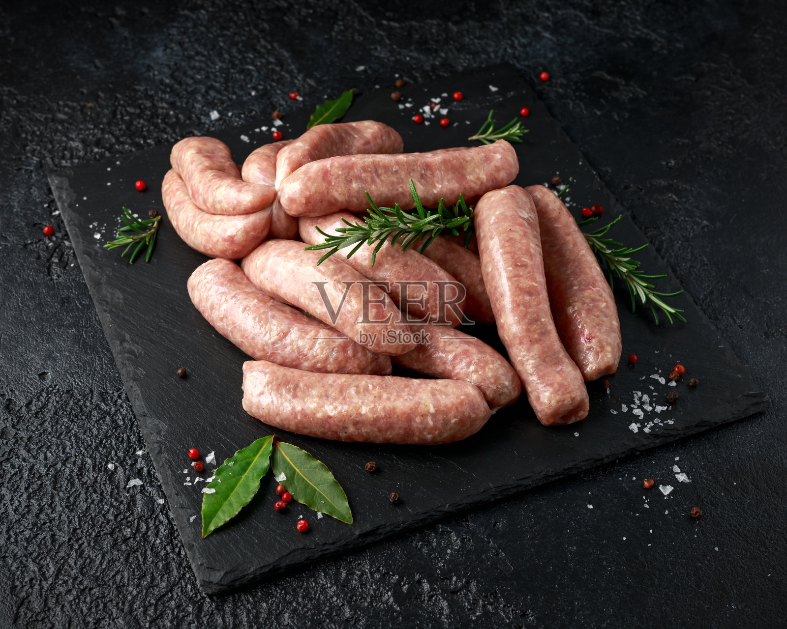 刚做的生肉屠夫用皮包着香肠，石板上放着香草照片摄影图片