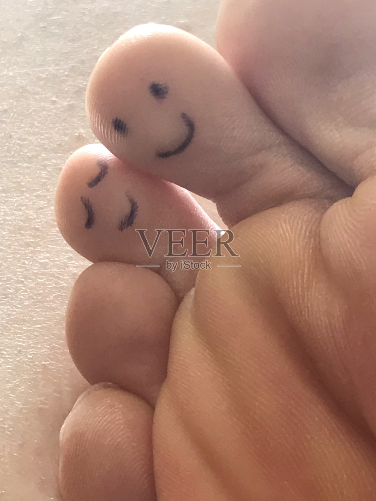 一个男人的脚从下面的表情符号笑脸和瞌睡的眼睛画在两个脚趾上，旁边的大脚趾，显示了脚的皮肤图案，脚趾与朋友的脸像表情纹身照片摄影图片