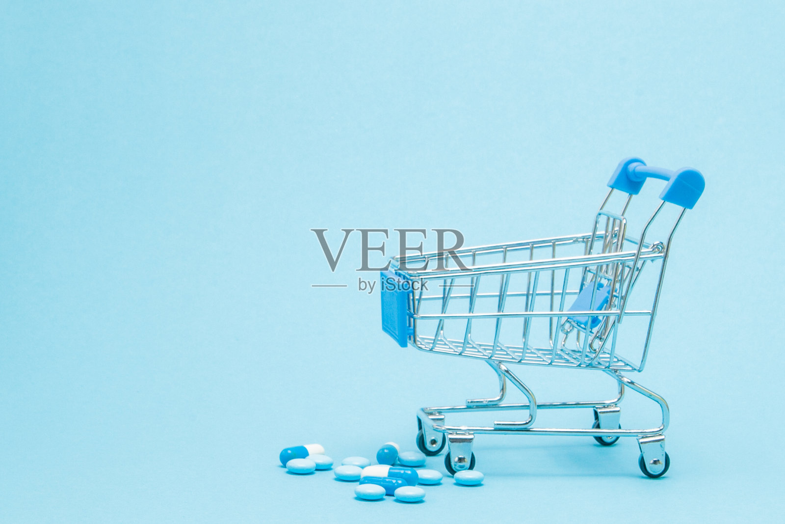 蓝色背景的药片和购物车。创意医疗成本、药店、健康保险和制药公司的经营理念。本空间照片摄影图片